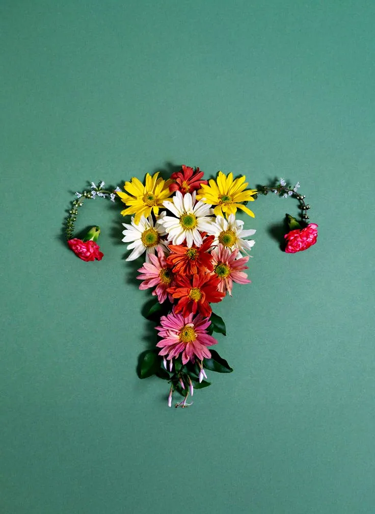 Flowers arranged in the shape of a uterus on a sage-green backdrop