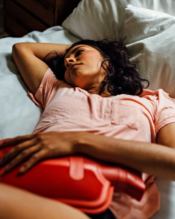 A woman lying in bed with a hot water bottle held against her abdomen