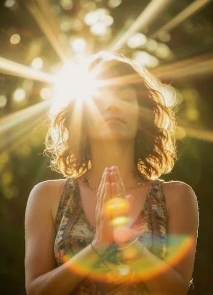 A woman standing in sunlight with her hands at her heart