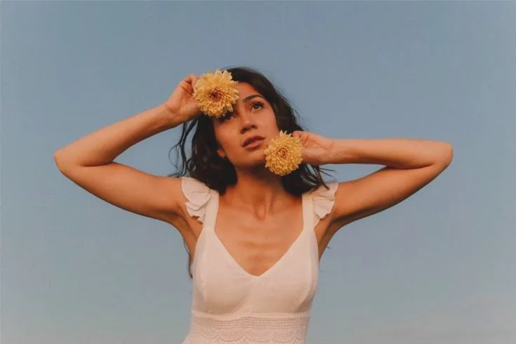 A woman holding yellow chrysanthemums beside her face against a clear sky
