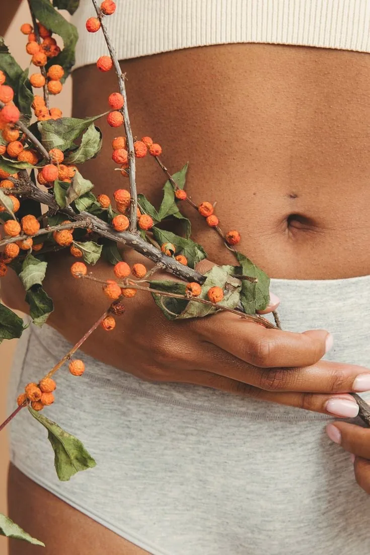 A woman holding a branch of orange berries against her midsection