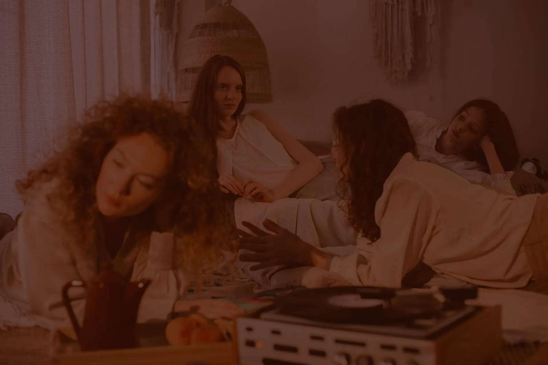Four women talking together on a bed in warm evening light