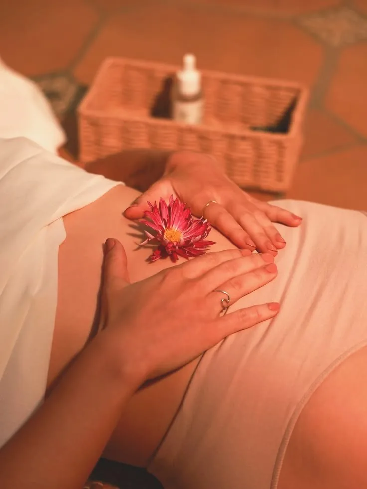 Hands resting on a woman's abdomen beside a single pink flower