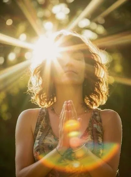 A woman with her hands at her heart, the sun flaring behind her